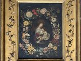 un tableau représentant une femme tenant un enfant dans ses bras, dans un cadre orné de fleurs