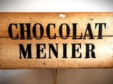une enseigne en bois sur laquelle est inscrit « Chocolate Menier »