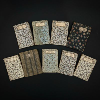 six petits cahiers sont alignés sur une surface noire