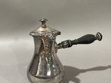 an antique silver coffee pot with a black handle on a white surface
