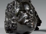 sculpture représentant une tête de femme posée sur une table à côté d'un vase