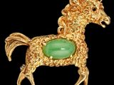 une image représentant une broche en forme de cheval, de couleur or et verte, sur fond noir