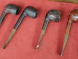 Plusieurs types de pipes à fumer sont alignés sur un support rouge