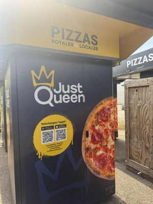 un distributeur automatique sur lequel est posée une pizza, devant un immeuble