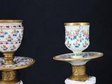 pair of antique porcelain cups and saucers on pedestals on a black background