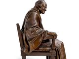 bronze statue of a man sitting on a bench with his legs crossed