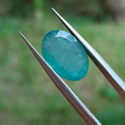 une personne tenant une pince sur laquelle est sertie une pierre bleue