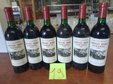 six bouteilles de vin rouge alignées sur une table, avec une étiquette de prix