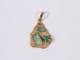a close up of a gold and green pendant on a white surface