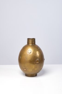 un vase doré posé sur une table blanche, près d'un mur blanc