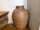 a brown vase sitting on the floor next to a stack of books