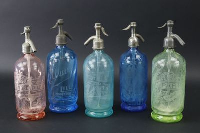 Quatre bouteilles en verre de couleurs différentes sont alignées sur une surface noire.