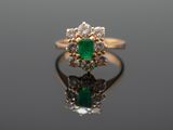 a close up of a gold ring with a green emerald and white diamonds