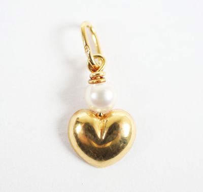 a close up of a gold heart charm with a pearl bead