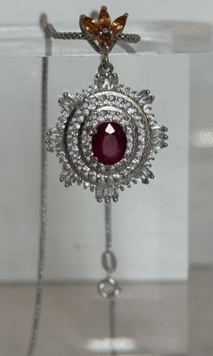 collier en argent orné d'une pierre rouge entourée de diamants sur un support
