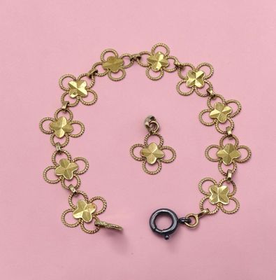a close up of a gold bracelet and earring on a pink background