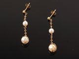 une paire de boucles d'oreilles en perles et en or posées sur un fond noir