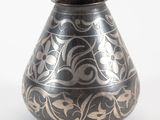 un vase noir et argenté posé sur une surface blanche