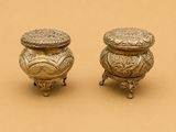 paire de petits pots anciens en métal argenté sur un socle, sur fond marron