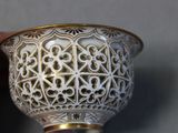 a hand holding a white and gold vase on a table