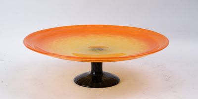 un plat à gâteau en verre orange posé sur un socle noir