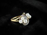 a gold ring with pearls and diamonds on a black background