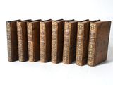 six old books are lined up in a row on a white surface