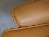 a close up of a brown leather chair with a white wall in the background