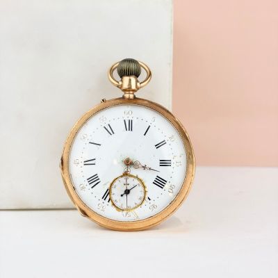 montre de poche en or avec des chiffres romains, posée sur un bloc de marbre