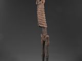 une statue en bois représentant un squelette au long cou et aux longs bras