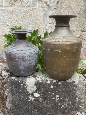 two vases sitting on top of a rock in front of a stone wall