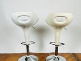 two white stools sitting on top of a wooden floor next to a white wall