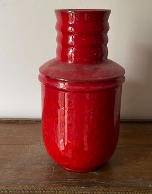 un vase rouge posé sur une table, avec un mur blanc en arrière-plan