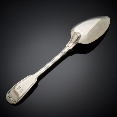 une cuillère ancienne en argent posée sur une surface noire, avec un fond noir