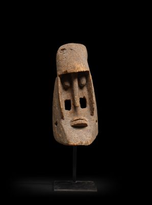 un masque en argile posé sur un socle, sur fond noir
