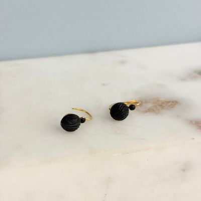 une paire de boucles d'oreilles noires et dorées posées sur une surface en marbre