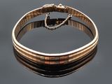 bracelet en or avec une chaîne et un fermoir posé sur une surface réfléchissante