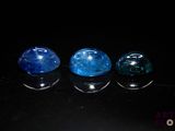 three blue and one green gems sitting on top of a black surface