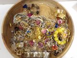 a wooden bowl filled with lots of gold and silver jewelry