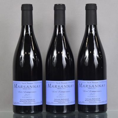 three bottles of wine sit on a glass table in front of a gray wall