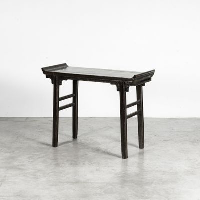 une table en bois noir avec un plateau en verre, posée sur un sol en ciment