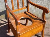a wooden chair with a potty seat in front of a concrete wall