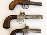 trois vieux revolvers sont alignés sur une surface blanche