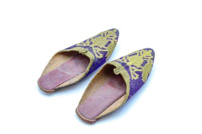 une paire de pantoufles violettes et dorées posées sur une surface blanche