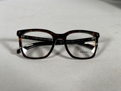 Lunettes Prada à monture écaille avec verres transparents, posées sur une surface blanche