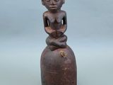 une vieille statue en bois représentant un homme assis au sommet d'une cloche