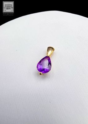 un gros plan d'un pendentif violet en forme de larme posé sur une surface blanche