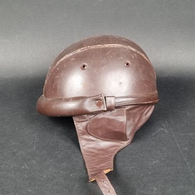un vieux casque en cuir muni d'une lanière en cuir, posé sur une surface noire