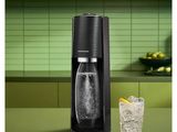 une machine à soda posée sur un plan de travail, à côté d'un verre de soda