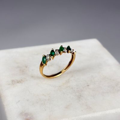un gros plan d'une bague en or sertie de pierres vertes posée sur une surface en marbre